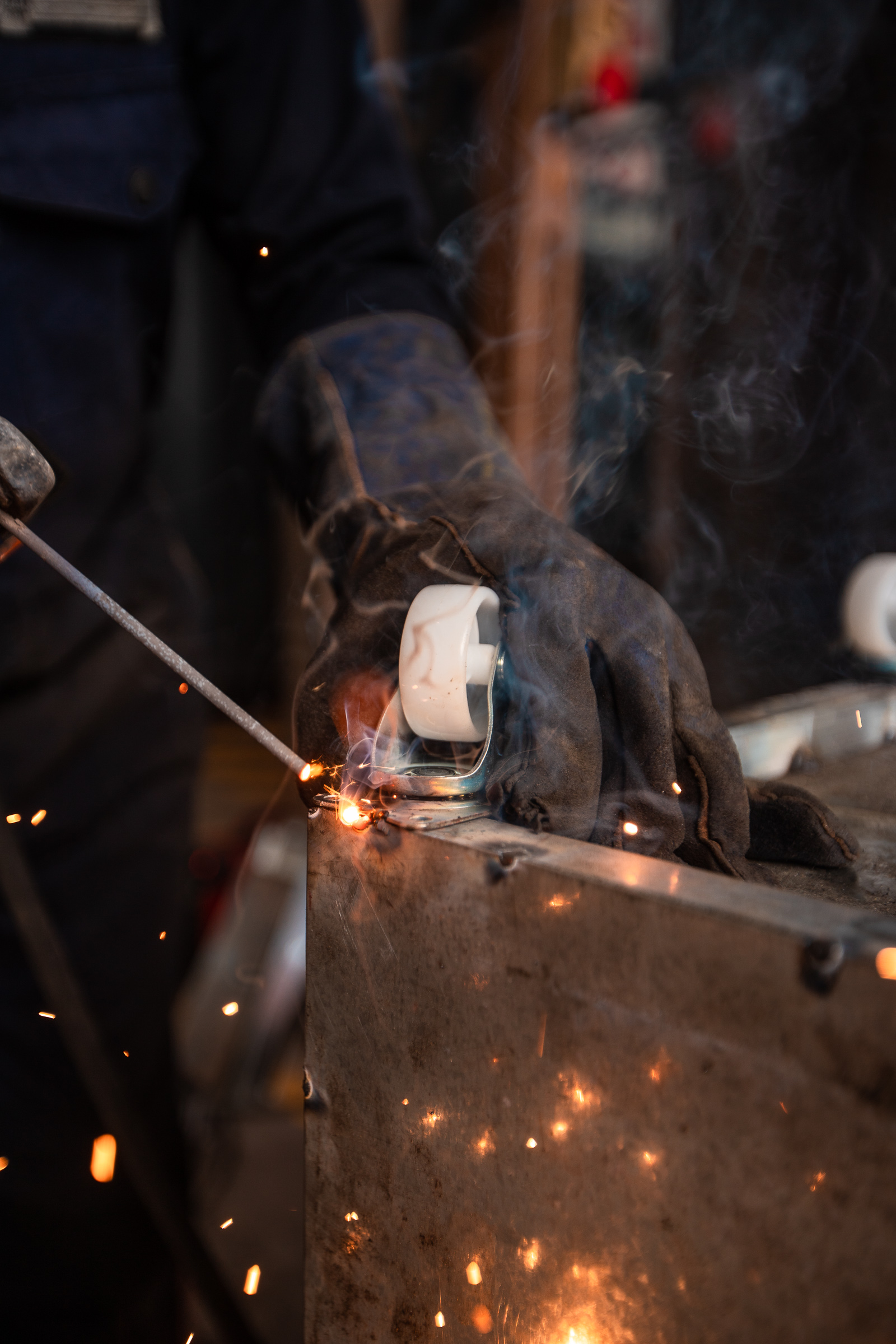 Close view of a gloved welder joining steel with a welding rod, sparks falling from the joint