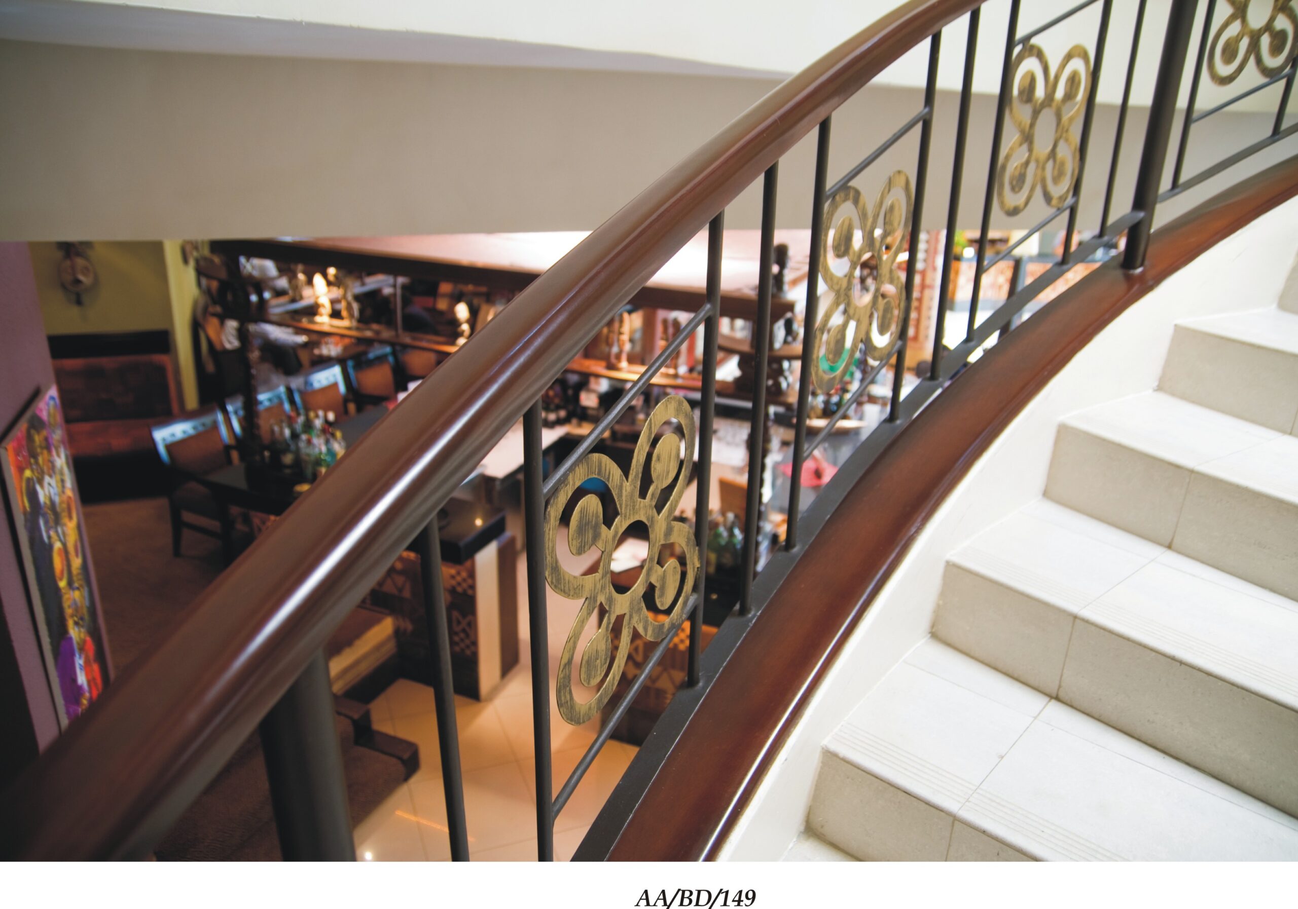 Curved wrought iron balustrade with gold scroll panels following a staircase with a timber handrail