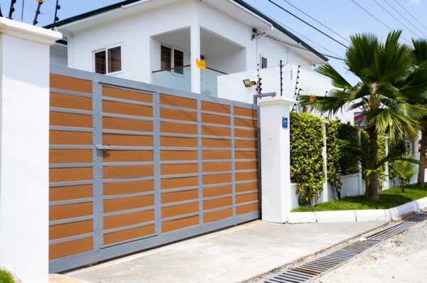 Finished steel sliding driveway gate with timber effect slats set between white boundary pillars