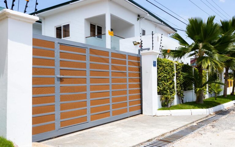 Finished steel sliding driveway gate with timber effect slats set between white boundary pillars