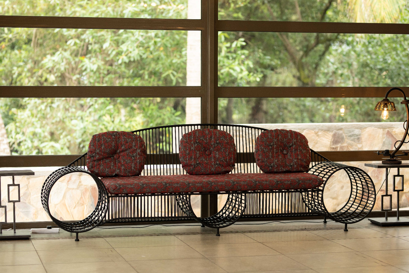 Wrought iron sofa with circular wire arms and red cushions in front of a garden window